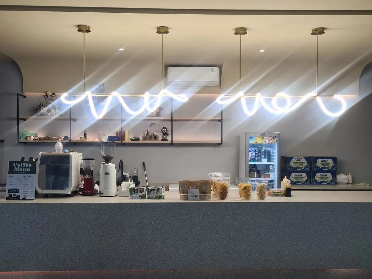 The café counter at Glass House Padel with its neon script sign