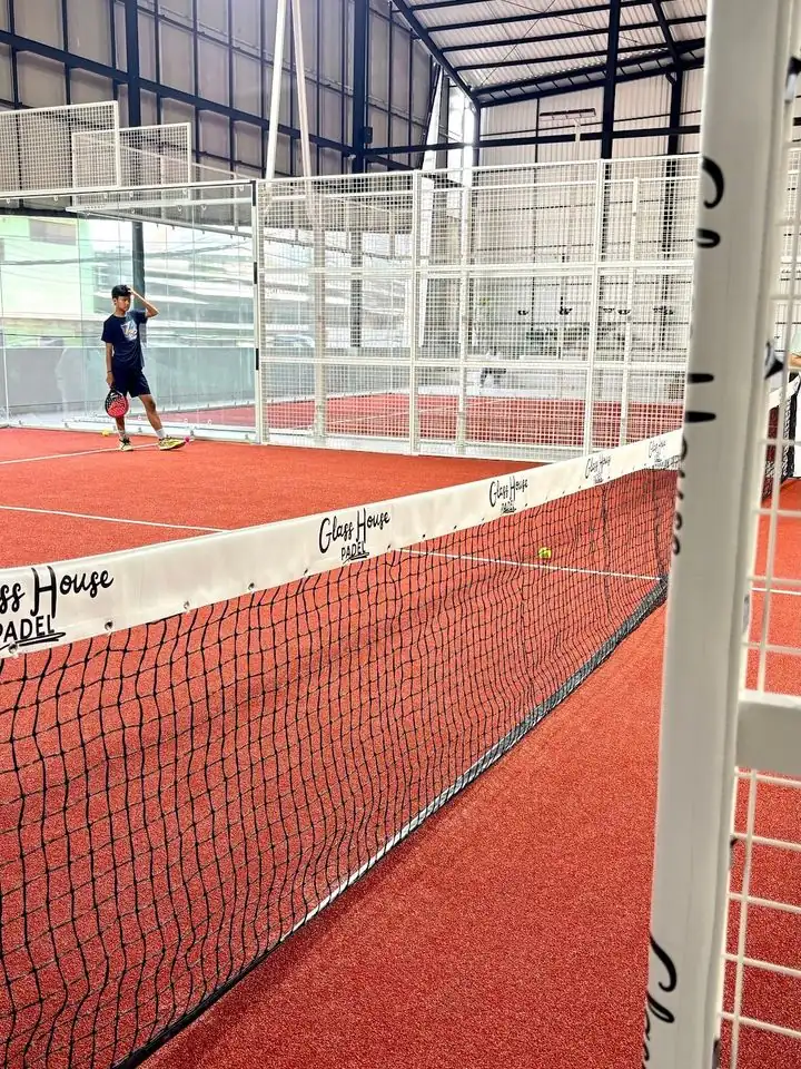 Players on the clay-red court at Glass House Padel