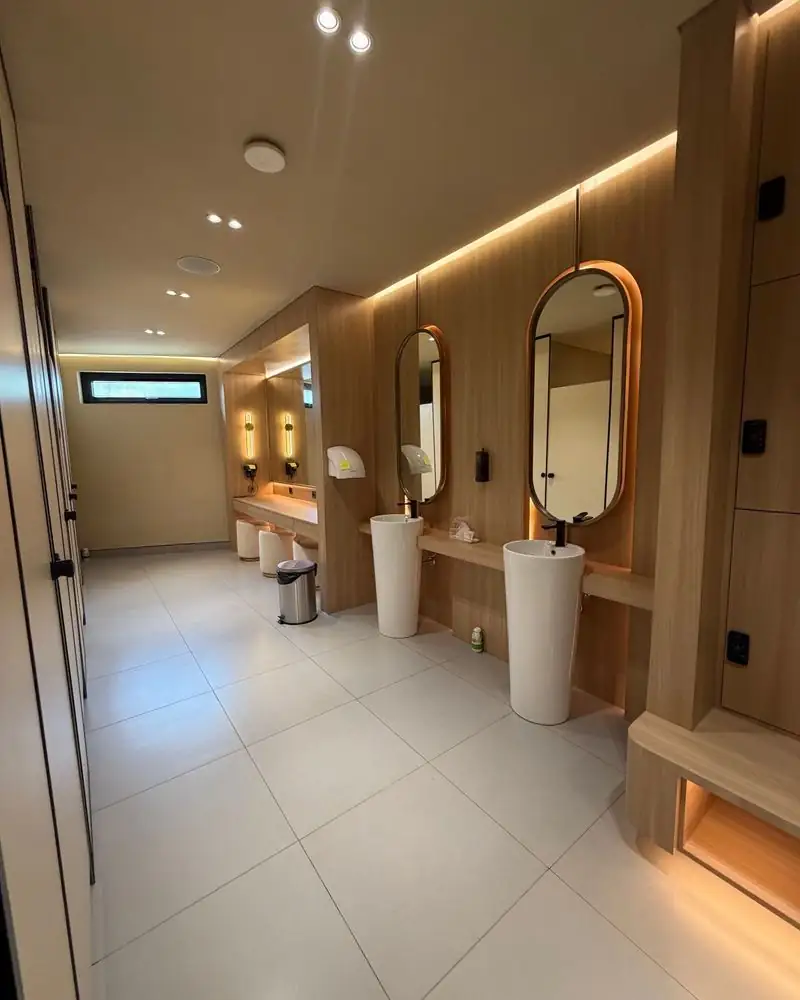 Warm oak changing room with pill-shaped mirrors at Glass House Padel